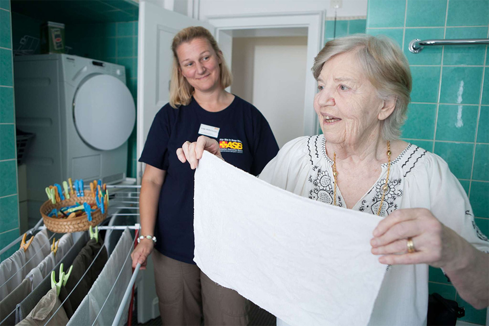 Eine ASB-Mitarbeiterin hilf einer Seniorin beim Wäschewaschen.