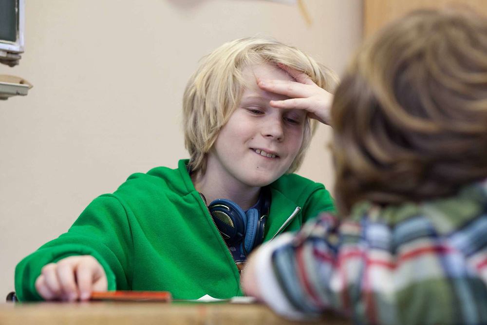 Ein Schüler sitzt an einer Schulbank und stützt den Kopf ab.